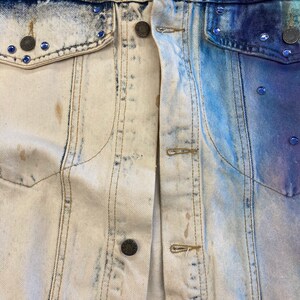 May include: A denim jacket with a light blue and white bleached design. The jacket has a button closure and two pockets on the front.