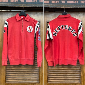 May include: Red long-sleeve shirt with white and black stripes on the sleeves. The shirt has a zipper closure and a small patch on the right chest that says "Santa Rosa Neptunes". The back of the shirt has "NEPTUNES" written in black letters.