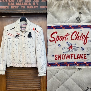 Könnte beinhalten: Eine cremefarbene Vintage-Jacke mit Reißverschluss, die ein Skifahrer- und Baumdesign sowie Schneeflockenmuster aufweist. Die Jacke hat ein "Sport Chief"-Etikett mit dem Wort "SNOWFLAKE".