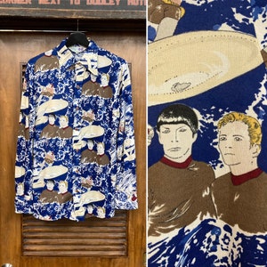 Puede incluir: Una camisa azul de manga larga con botones con un patrón repetido de personajes de Star Trek y platillos voladores.