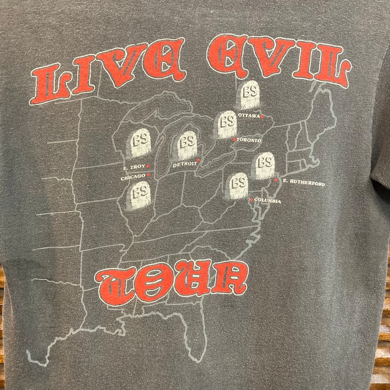 May include: A gray t-shirt with a map of the United States printed on the front. The map shows the locations of various cities where the band Live Evil toured. The text "LIVE EVIL TOUR" is printed in red letters on the map.