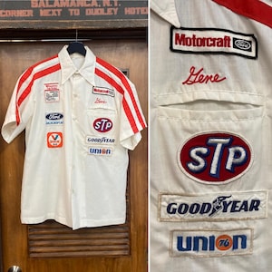 May include: A white short-sleeve button-down shirt featuring red stripes on the shoulders and various embroidered patches including Motorcraft, Ford, STP, Goodyear, and Union 76. The name Gene is embroidered in red script above the chest pocket.