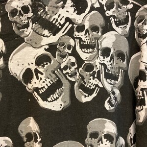 Puede incluir: Patr&oacute;n de calaveras blancas y negras sobre una tela. Las calaveras est&aacute;n en varios tama&ntilde;os y posiciones, algunas se superponen. El fondo es negro.