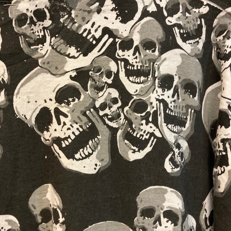 Puede incluir: Patr&oacute;n de calaveras blancas y negras sobre una tela. Las calaveras est&aacute;n en varios tama&ntilde;os y posiciones, algunas se superponen. El fondo es negro.
