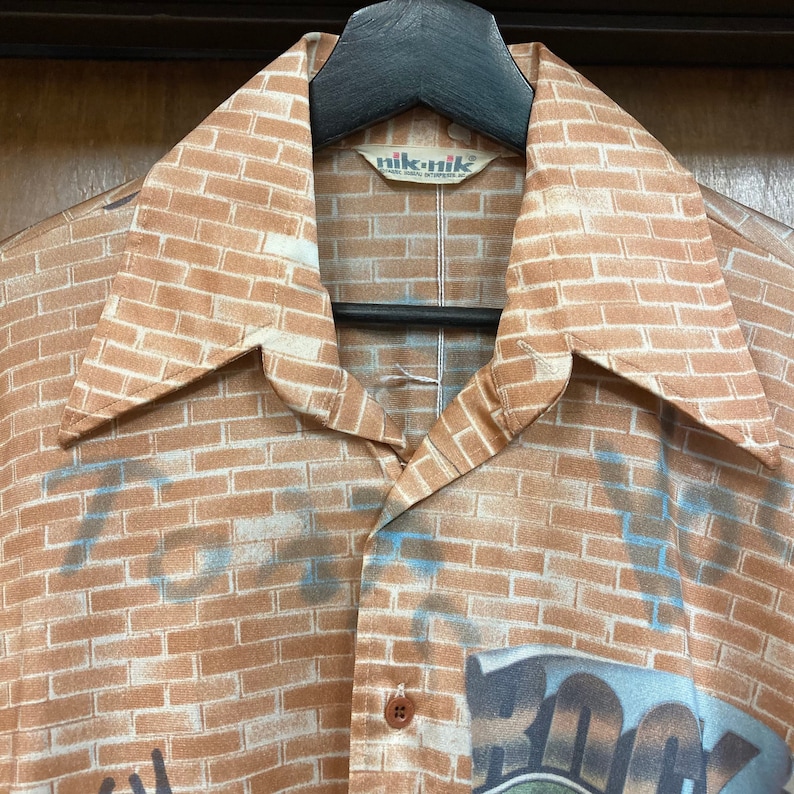 May include: A brown and white brick patterned shirt with a collar and a button closure. The shirt has the text "nik-nik" on the label.