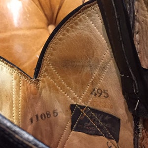 Pu&ograve; includere: Primo piano dell'interno di uno stivale in pelle marrone con cuciture e i numeri 495 e 11085 visibili. &Egrave; anche visibile un'etichetta in pelle nera con il testo "Justin Boots".