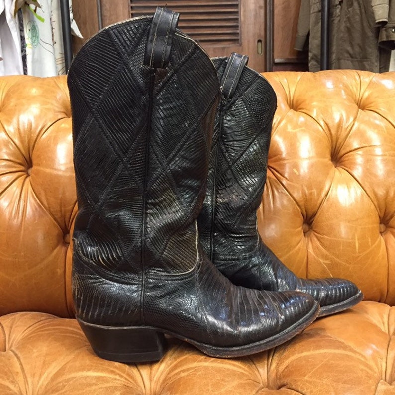 Pu&ograve; includere: Un paio di stivali da cowboy in pelle nera con un motivo a rombi. Gli stivali hanno una punta a punta e un tacco basso.