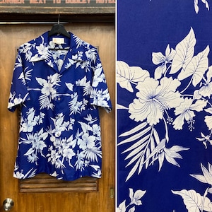 Peut inclure: Une chemise à manches courtes boutonnée d'un bleu roi vif avec un imprimé floral blanc répétitif composé de fleurs d'hibiscus et de feuilles tropicales. La chemise présente un col classique, une poche poitrine et une fermeture boutonnée.