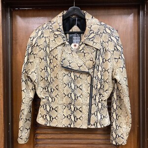 Puede incluir: Una chaqueta de cuero con estampado de piel de serpiente beige y negro con cierre de cremallera. La chaqueta tiene una etiqueta de North Beach.