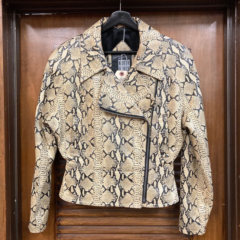 Puede incluir: Una chaqueta de cuero con estampado de piel de serpiente beige y negro con cierre de cremallera. La chaqueta tiene una etiqueta de North Beach.