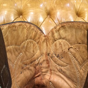 K&ouml;nnte beinhalten: Nahaufnahme des Innenraums eines braunen Leder-Cowboystickels. Der Stiefel ist mit "Texas" beschriftet und hat die Gr&ouml;&szlig;en- und Stilnummer "10 1/2 9744" auf der Innenseite.