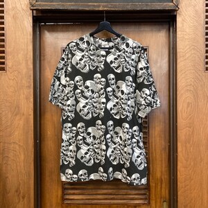 Puede incluir: Camiseta negra de manga corta con un estampado de calaveras. Las calaveras son blancas y grises y est&aacute;n dispuestas en un patr&oacute;n aleatorio.
