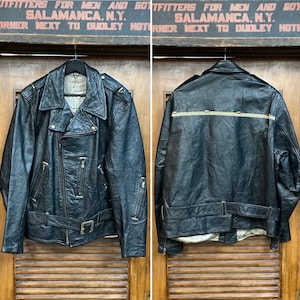 May include: Black leather motorcycle jacket with a belted waist, asymmetrical zipper, and multiple pockets. The jacket has a classic biker style with a notched collar and shoulder epaulets. The back features a horizontal stripe detail. The jacket is hanging on a wooden door.
