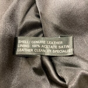 Puede incluir: Una etiqueta de chaqueta de cuero negra con el texto "SHELL: GENUINE LEATHER LINING: 100% ACETATE SATIN LEATHER CLEAN BY SPECIALIST"