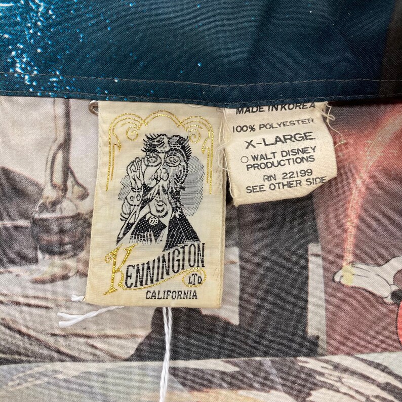 May include: A white tag with gold lettering that reads "Kennington Ltd. California" and a cartoon image of a man with a magnifying glass. The tag is attached to a blue and white shirt with a tag that reads "Made in Korea, 100% Polyester, X-Large, Walt Disney Productions, RN 22199, See Other Side."