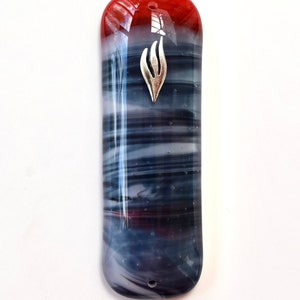 May include: A rectangular glass mezuzah case with a red top and a blue and white swirled design. A silver-colored metal emblem is affixed to the front. The case has a hole at the top for hanging.