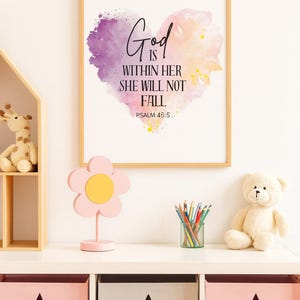 May include: A framed print with the text "God is within her she will not fall" over a watercolor heart. A pink flower-shaped decor, a teddy bear, and storage cubes with star cutouts are on a white shelf.