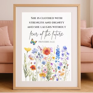 Può includere: Stampa artistica incorniciata con un design floreale ad acquerello e la citazione di Proverbi 31:25: "È rivestita di forza e dignità e ride senza paura del futuro." L'opera presenta fiori colorati e una farfalla.