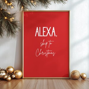 Könnte beinhalten: Ein gerahmter roter Druck mit dem Text "ALEXA, skip to Christmas" in Weiß. Der Druck befindet sich in einem goldenen Rahmen und ist mit goldenen Ornamenten und Weihnachtsgrün geschmückt.