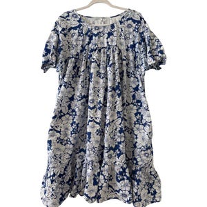 May include: A blue and white floral print dress with short sleeves and a ruffled hem. The dress is hanging on a white hanger. The floral pattern features large white flowers against a dark blue background.