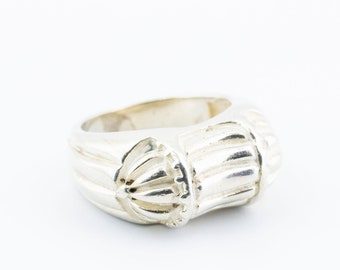 May include: A silver ring with a textured, ridged design. The ring is wide and has a rounded shape.