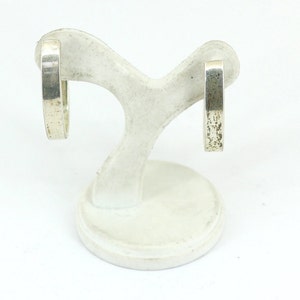 May include: A pair of silver hoop earrings on a white display stand. The earrings are simple and have a smooth, polished finish.