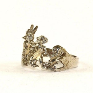 Op de afbeelding: Een zilveren ring met een gedetailleerd ontwerp van twee figuren die op een paard rijden. De ring is gemaakt van sterling zilver en heeft een getextureerde afwerking.