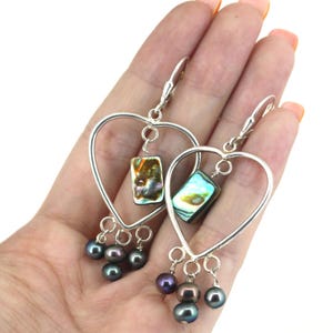 May include: Silver heart shaped earrings with iridescent abalone shell accents and black pearls dangling from the bottom.