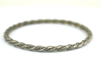 Könnte beinhalten: Ein silbernes, gedrehtes Armkettchen. Das Armband besteht aus einem einzigen Stück Metall, das zu einem seilartigen Design gedreht ist.