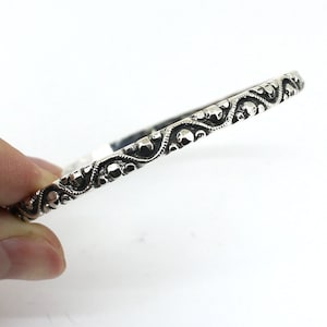 May include: A silver bangle bracelet with a detailed, intricate design. The design features a repeating pattern of swirls and dots.