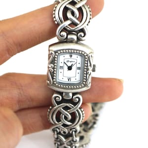 May include: A white ceramic mug with a black handle and the text "But First, Coffee" in a black, bold font. The mug is on a white surface. The mug is approximately 4 inches tall.