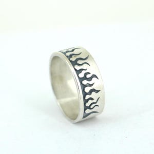 May include: A silver band ring with a black flame design around the band.