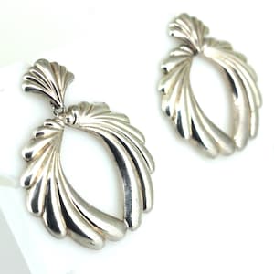 May include: A pair of silver dangle earrings with a fan-shaped design. The earrings are made of smooth, polished metal and have a modern, geometric look.