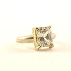 May include: A silver ring with a large, clear, square-shaped gemstone.