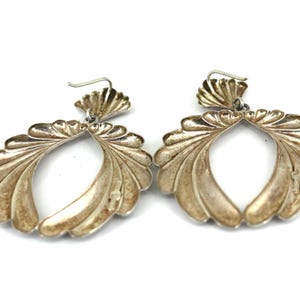 May include: A pair of silver earrings with a scallop shell design. The earrings are large and dangle from the earlobe.