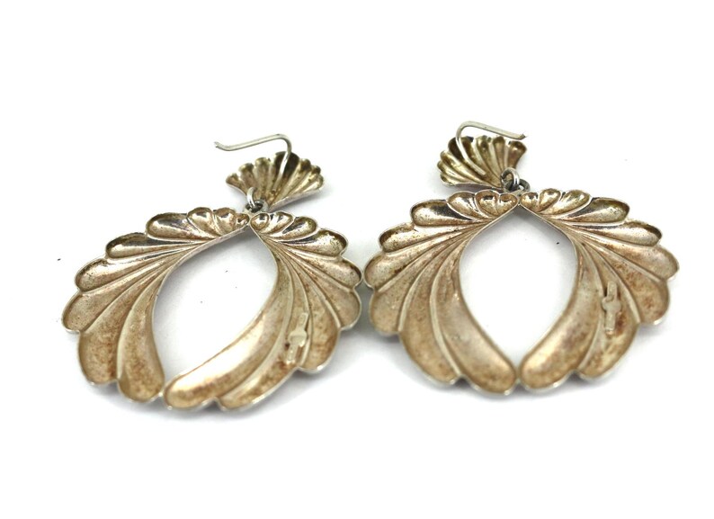 May include: A pair of silver earrings with a scallop shell design. The earrings are large and dangle from the earlobe.
