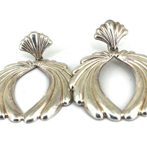 May include: A pair of silver earrings with a fan-shaped design. The earrings are oval-shaped and have a scalloped top.