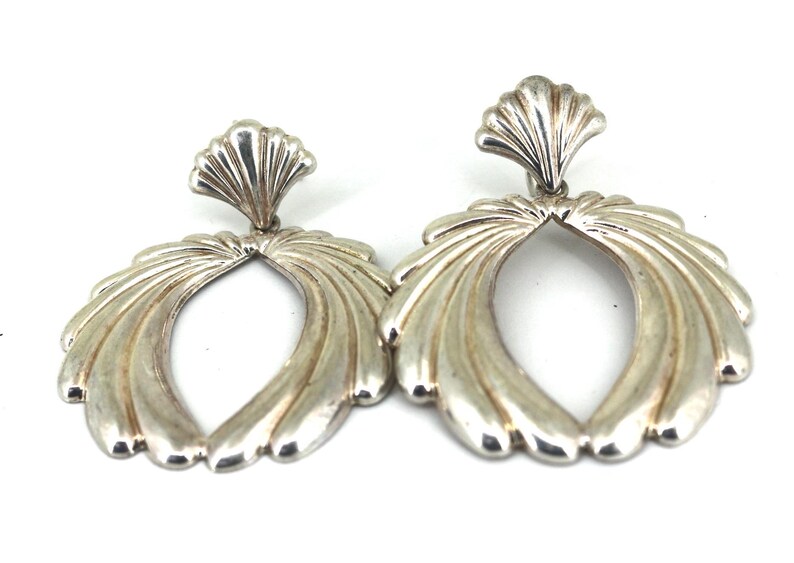May include: A pair of silver earrings with a fan-shaped design. The earrings are oval-shaped and have a scalloped top.