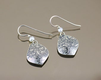 May include: A pair of silver dangle earrings with a white pearl accent. The earrings feature a teardrop-shaped pendant with a black and white paisley design.