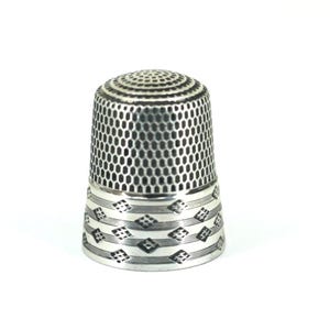 Puede incluir: Un dedal de metal de color plateado con un patrón de panal texturizado en la cúpula superior y los lados. La base del dedal está decorada con una banda horizontal de líneas grabadas y pequeños motivos en forma de diamante que se repiten.