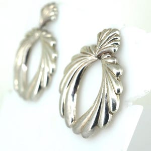 May include: A pair of silver earrings with a unique, fan-shaped design. The earrings are oval-shaped with a textured, wavy surface.