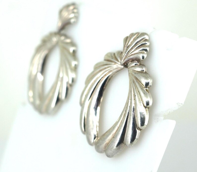 May include: A pair of silver earrings with a unique, fan-shaped design. The earrings are oval-shaped with a textured, wavy surface.