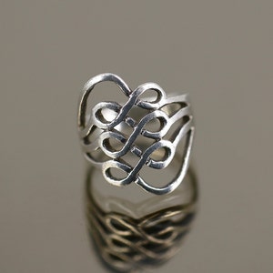 Puede incluir: Un anillo de plata con un diseño de nudo celta. El anillo está hecho de una sola pieza de metal que se retuerce y entrelaza para crear un patrón complejo.