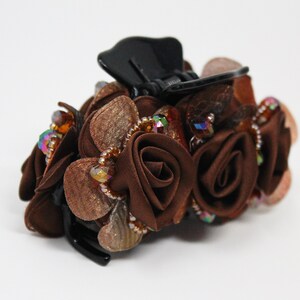 Może przedstawiać: Brązowa spinka do włos&oacute;w z czarną podstawą i skupiskiem brązowych r&oacute;ż z tkaniny ozdobionych tęczowymi koralikami.