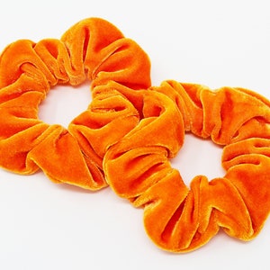 Puede incluir: Dos scrunchies de terciopelo naranja. Los scrunchies están hechos de un tejido suave y elástico, perfecto para sujetar el cabello en su lugar.
