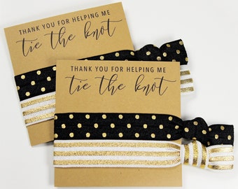 May include: Two sets of black and gold hair ties with cards that read "THANK YOU FOR HELPING ME tie the knot." One set features gold polka dots, the other gold stripes. The cards are brown.