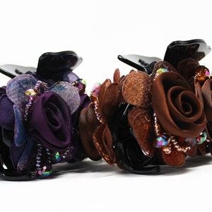 Może przedstawiać: Dwa spinki do włos&oacute;w z kwiatowym wzorem. Jedna spinka jest fioletowa, a druga brązowa. Obie spinki mają kryształki i są wykonane z tkaniny.