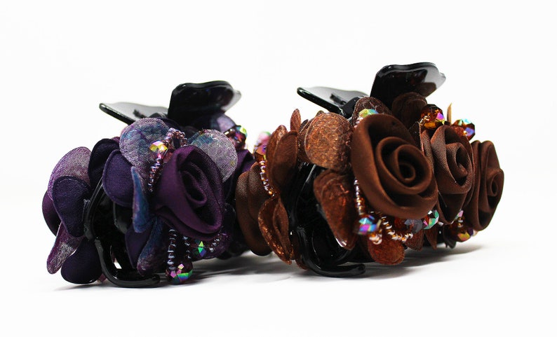 Może przedstawiać: Dwa spinki do włos&oacute;w z kwiatowym wzorem. Jedna spinka jest fioletowa, a druga brązowa. Obie spinki mają kryształki i są wykonane z tkaniny.