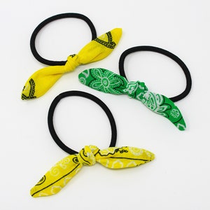 Puede incluir: Tres coleteros con lazos de tela. Un coletero tiene un lazo amarillo con un estampado paisley blanco, y los otros dos coleteros tienen lazos verdes con estampados paisley blancos.