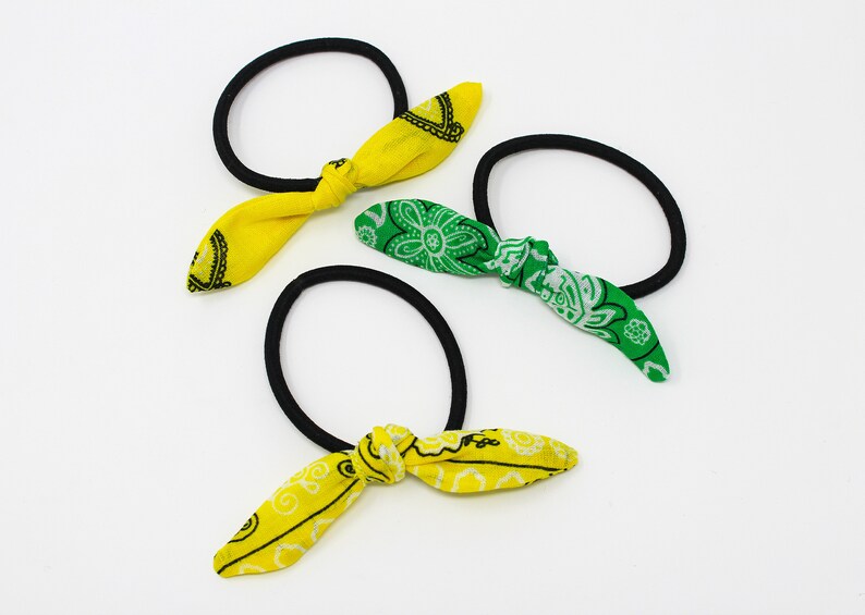 Puede incluir: Tres coleteros con lazos de tela. Un coletero tiene un lazo amarillo con un estampado paisley blanco, y los otros dos coleteros tienen lazos verdes con estampados paisley blancos.
